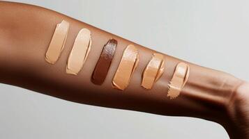 Various foundation shades are applied on a model's arm, highlighting a range of colors that suit different skin tones. The swatches are arranged in a straight line for easy comparison. photo