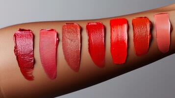 Different lip colors are applied on an arm, displaying a gradient from rich reds to subtle pinks. The colors vary in saturation and finish, showcasing diverse styling options. photo