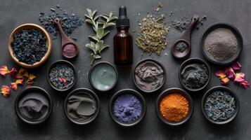 An assortment of vibrant herbs and powders is neatly arranged in bowls on a dark surface, showcasing various colors and textures. An aromatic oil bottle is included among the natural ingredients. photo
