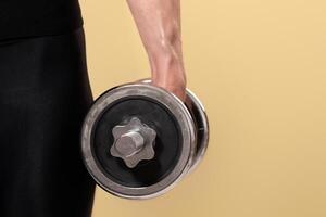 Middle aged fitness blogger and popular trainer and ad space. Hand of muscular adult female doing dumbbell exercise, isolated on beige background, empty space, close up, cropped, studio shot photo