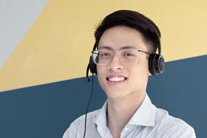 Portrait of Asian male helpdesk operator posing and smiling at call centre. Customer support agent with his diverse team working at modern open space office. Telecommunications concept photo