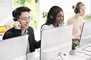 Team of helpline operators with headsets consulting clients at call center. Millennial customer service representatives working online in telemarketing at modern open space office photo