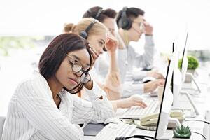 Overworked female helpline consultant procrastinating near computer monitor at call centre, blank space. Tired African American tech support agent feeling stressed at workplace photo