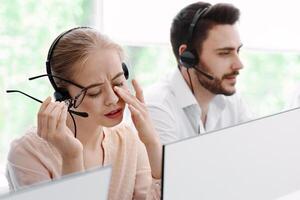 Overworked hotline operator in front of computer monitor and her busy coworkers at call centre office photo