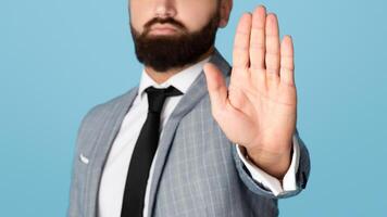 Cropped view of millennial businessman refusing something, showing STOP gesture on blue studio background. Unrecognizable young manager expressing his disapproval or denial photo