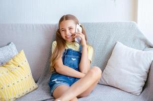 Pleasant Talk With Friend. Portrait of happy girl talking on smart phone sitting on the beige sofa with pillows photo