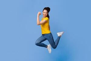 Overjoyed asian girl jumping in the air, celebrating success with raised fists over purple studio background, full-length shot, free space photo
