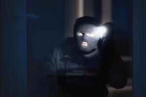 Spying Concept. Burglar in black balaclava hat watching what's inside the building in the night, using torch photo