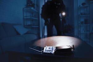 Burglary Concept. Robber breaking into residential building, using flash light on cash and smart phone lying on the table photo