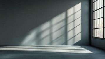 Sunlight streams into an empty loft through large window casting shadows. The walls are gray and the floor is concrete. photo