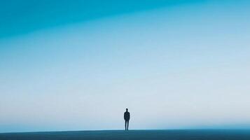 A lone figure stands against a vast blue sky, creating a powerful contrast that emphasizes the sense of isolation and introspection. The horizon stretches endlessly into the distance. photo