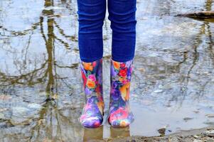 Women's legs in blue jeans and floral rubber boots in the puddle with reflection photo