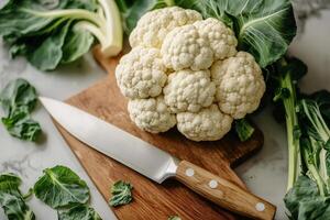 Chef preparing fresh cauliflower on wooden cutting board with sharp knife photo