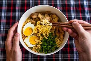 Piece of chicken in chopsticks with japanese ramen and male hands photo