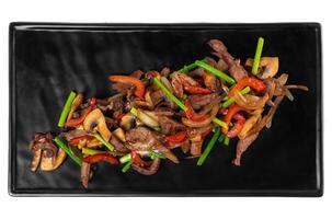Fried pork and beef with garlic arrows mushrooms and vegetables on a black plate on a white background photo
