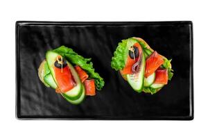 sandwiches with slice of tender smoked salmon and vegetables on a black plate on a white background top view photo