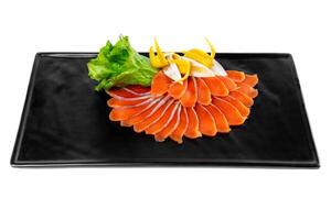 slicing appetizer of red fish slices on a black plate on a white background top view photo