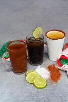 Mexican drinks Charro Negro, Jarrito, Cerveza roja on a gray table with salt pepper and lime photo