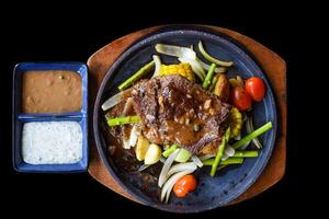 Roasted fire beef steak with vegetables and greens on plate isolated on black background top view photo