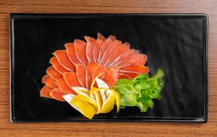 slicing appetizer of red fish slice on a black plate on a wooden table top view photo