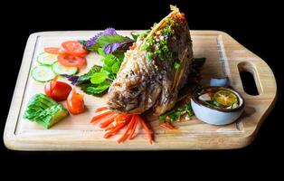 Red perch grilled in batter with vegetable and greens on wooden chop board isolated on black background top view photo