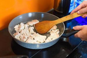 Hands with spatula stir fried chicken in a frying pan for preparing japanese ramen photo