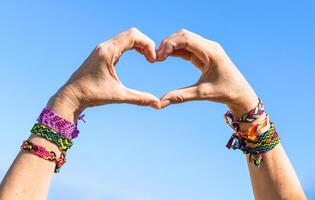 Hands making heart symbol on sky background. friendship bracelets on wrists photo