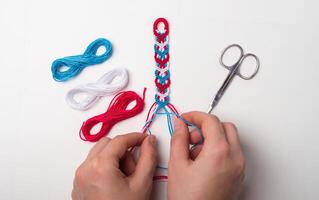 Process of weaving knot for DIY friendship bracelet Female hands. step by step. White background with copy space, scissors and thread photo