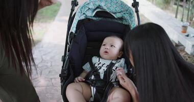 Handheld selective focus shot, Two Asian women play with a little boy in a baby stroller outside a coffee shop. A relaxing atmosphere with a warm moment video
