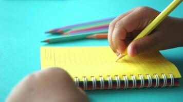 Child coloring in notepad with colored pencils on blue background video