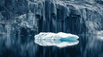 Iceberg floating on dark water with cliffs in background photo