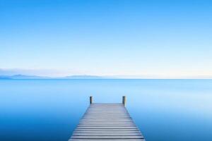 Wooden dock extends into calm, blue waters under a clear sky, mountains visible on the horizon photo
