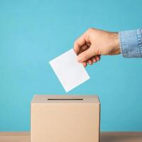 Hand placing a ballot in a box against a blue background, symbolizing voting and civic engagement photo