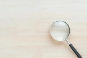 Close-up shot of a magnifying glass resting on a light, textured wooden surface, top-down view photo