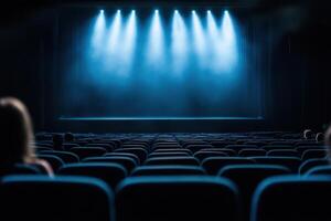 An empty theatre with its chairs is illuminated with a row of spotlights overhead the stage photo