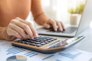 Calculating finances, Woman using calculator and laptop, analyzing charts for accounting tasks photo