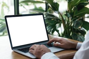 Person working on laptop with blank screen in bright workspace with greenery in background photo