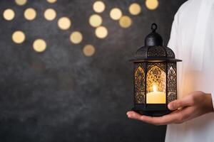 Ornate lantern glowing softly in a person's hands against a dark background with bokeh lights photo