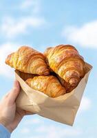 Freshly baked golden croissants in a paper bag against a blue sky backdrop. A delightful treat photo