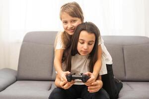 Two little girlfriends playing video game with joysticks. Excited and focused european children. Childhood concept. Entertainment and leisure. Idea of friendship. Grey background in studio. Copy space photo