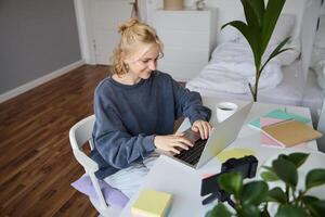 Portrait of young woman distance learning, working from home with laptop, making notes, student studying on remote, doing online course photo