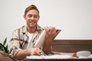 Portrait of tourist packing suitcase, going through check-list, writing down items to take with him in luggage, making notes in notebook, sitting on bed photo
