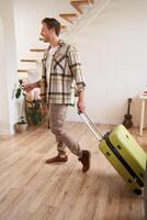 Full length photo of young man with suitcase, going on holiday trip, walking in flat, checking out from rented apartment