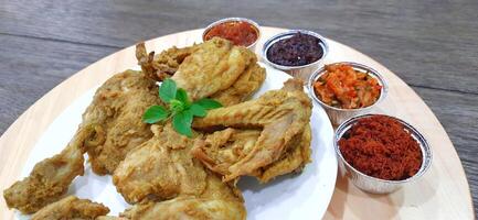 Ayam ungkep bumbu kuning or boiled chicken with curry seasoning and coconut water. Served with varian sambal or hot chili sauce. Ready to fried photo