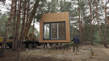 Installation of a Modern Prefabricated Cabin in a Forested Area During. The process involves precise maneuvering and placement of the structure onto a foundation amongst the tall pine trees. video
