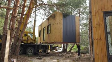 A crane lifts a prefabricated cabin into place in a wooded area. The cabin is made of wood and has a modern design. Process of constructing a small, off-grid home in a remote location. video