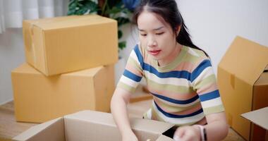 Handheld high angle view shot, Young asian woman packing her things into a cardboard box in preparation for moving to a new house. Moving and lifestyle concepts. video