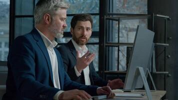 Two Caucasian men professional businessmen work together using computer in office discussing business project check financial data plan colleagues talking about marketing strategy corporate teamwork video