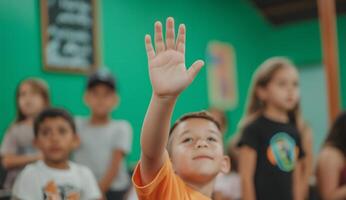 A young boy raises his hand in front of a classroom photo