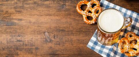 A frothy beer mug beside pretzels on a checkered cloth. photo